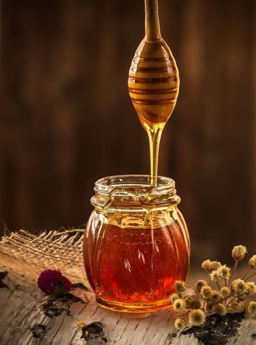 Honey drizzling from a dipper into a glass jar